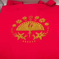 Full view of a red tote bag decorated with a gold glitter fan and floral design, displayed standing upright.