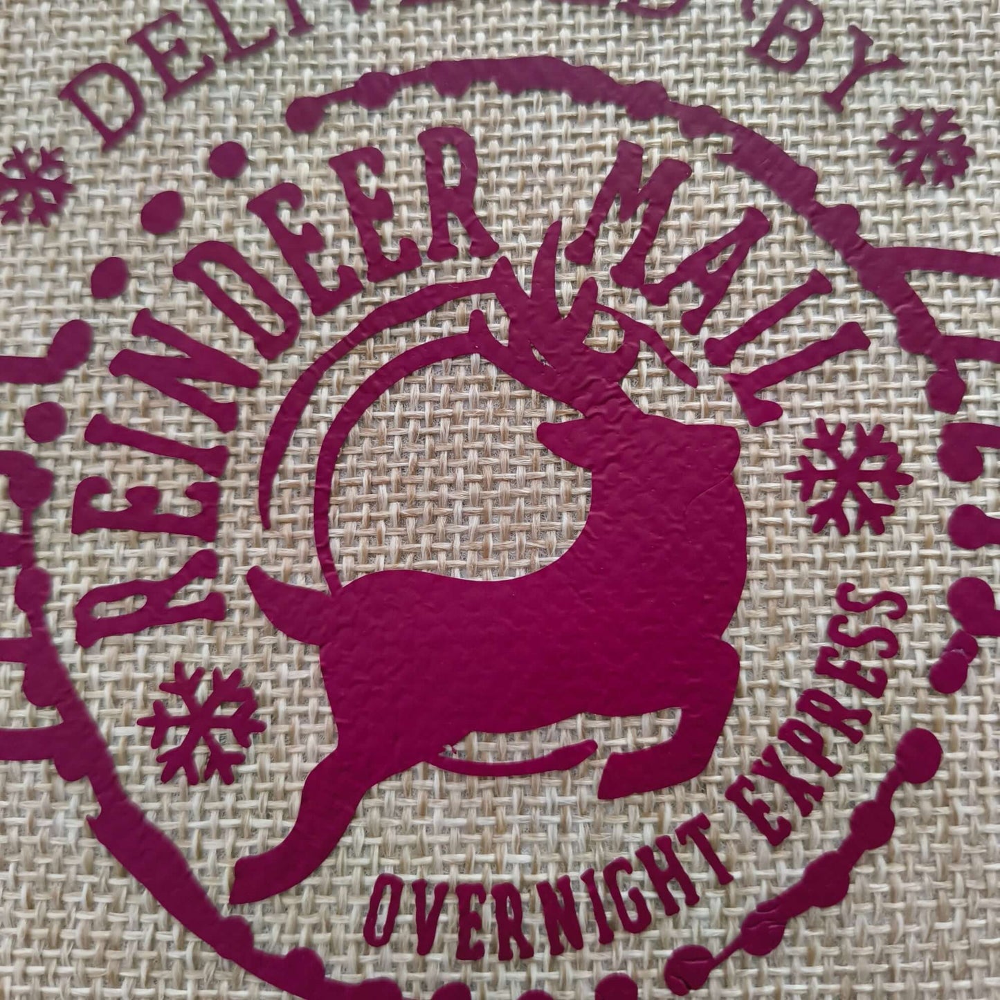 Detailed view of burgundy reindeer motif on rustic hessian Christmas gift bag with festive lettering.