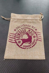 Hessian Christmas gift bag with burgundy "Delivered by Reindeer Mail Overnight Express" design, flat and empty on black background.