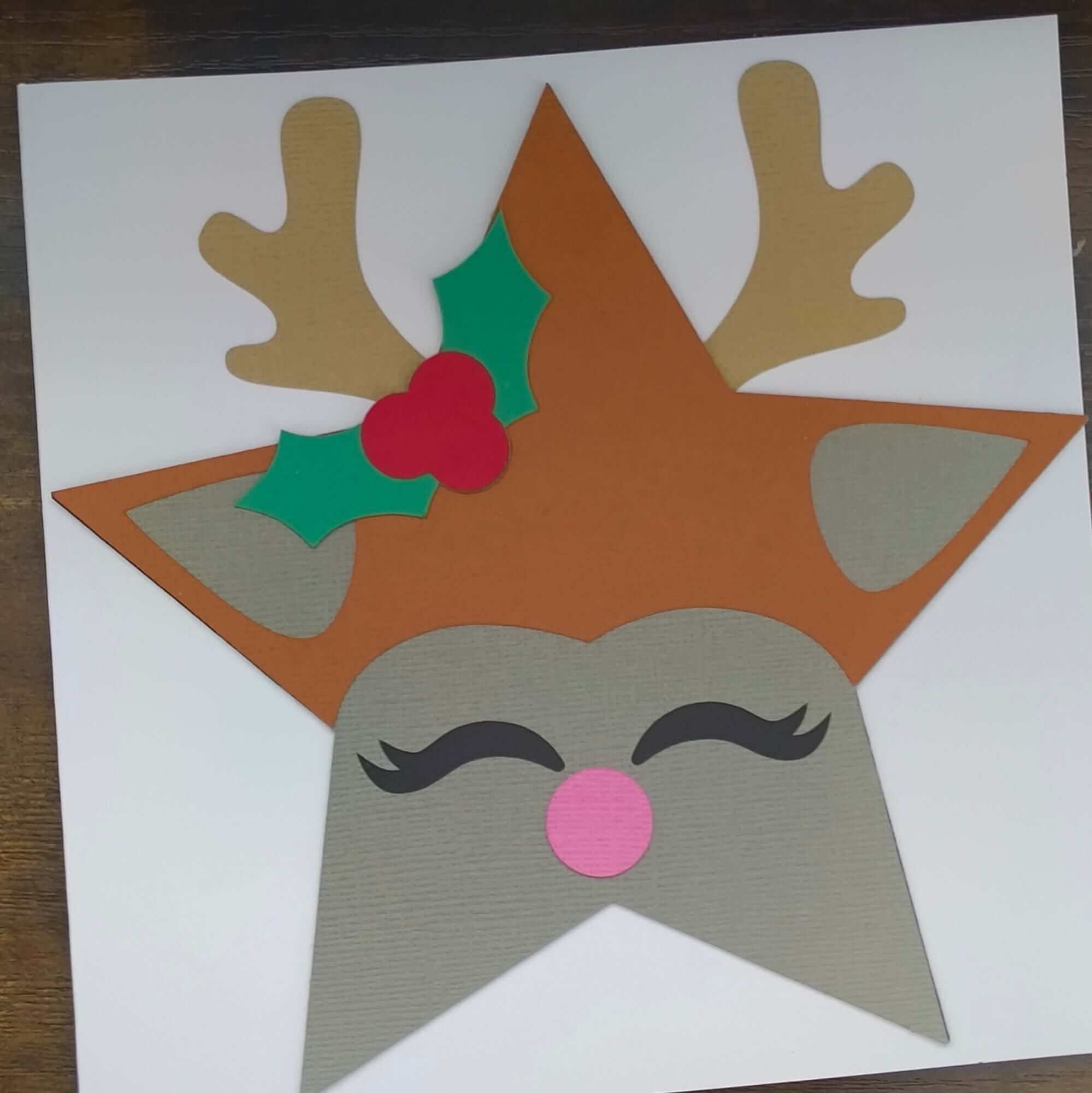 Handmade reindeer Christmas card featuring antlers, holly, and a pink nose in a star shape.