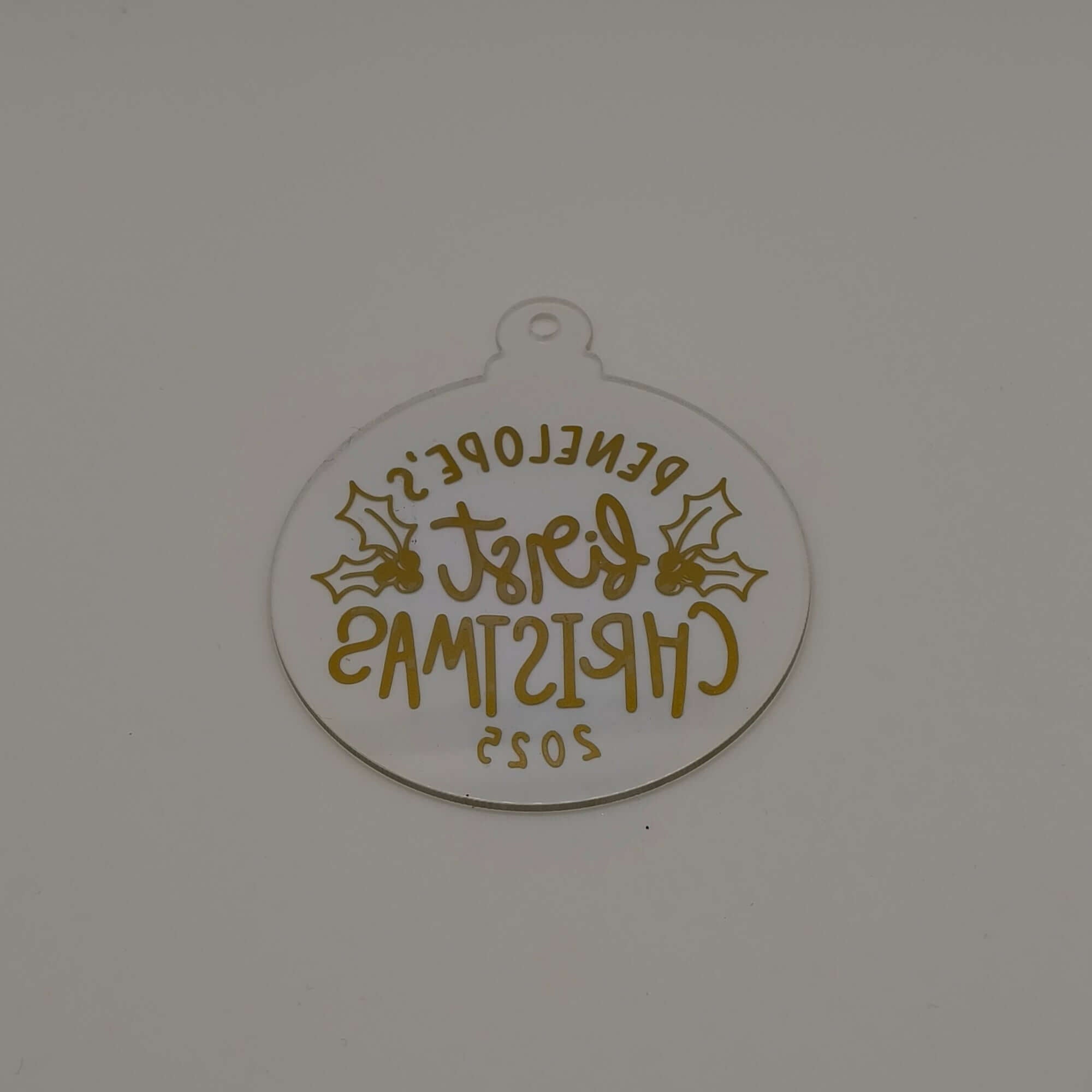 Reverse view of personalised gold and clear acrylic first Christmas bauble showing text from back.