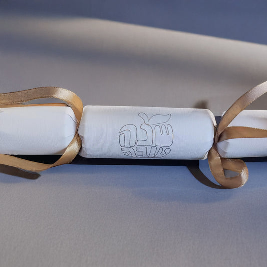 White cracker with gold foil Hebrew “Shana Tova” design and gold ribbon, displayed on a neutral background.
