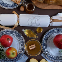 White cracker with “Shana Tova” foil design placed among traditional Rosh Hashanah foods including pomegranate, honey, and apples.

