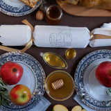 White cracker with “Shana Tova” foil design placed among traditional Rosh Hashanah foods including pomegranate, honey, and apples.

