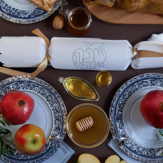White cracker with “Shana Tova” foil design placed among traditional Rosh Hashanah foods including pomegranate, honey, and apples.

