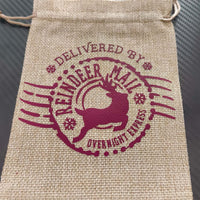 Hessian drawstring Christmas gift bag with festive reindeer mail print in burgundy, flat and ready for filling.