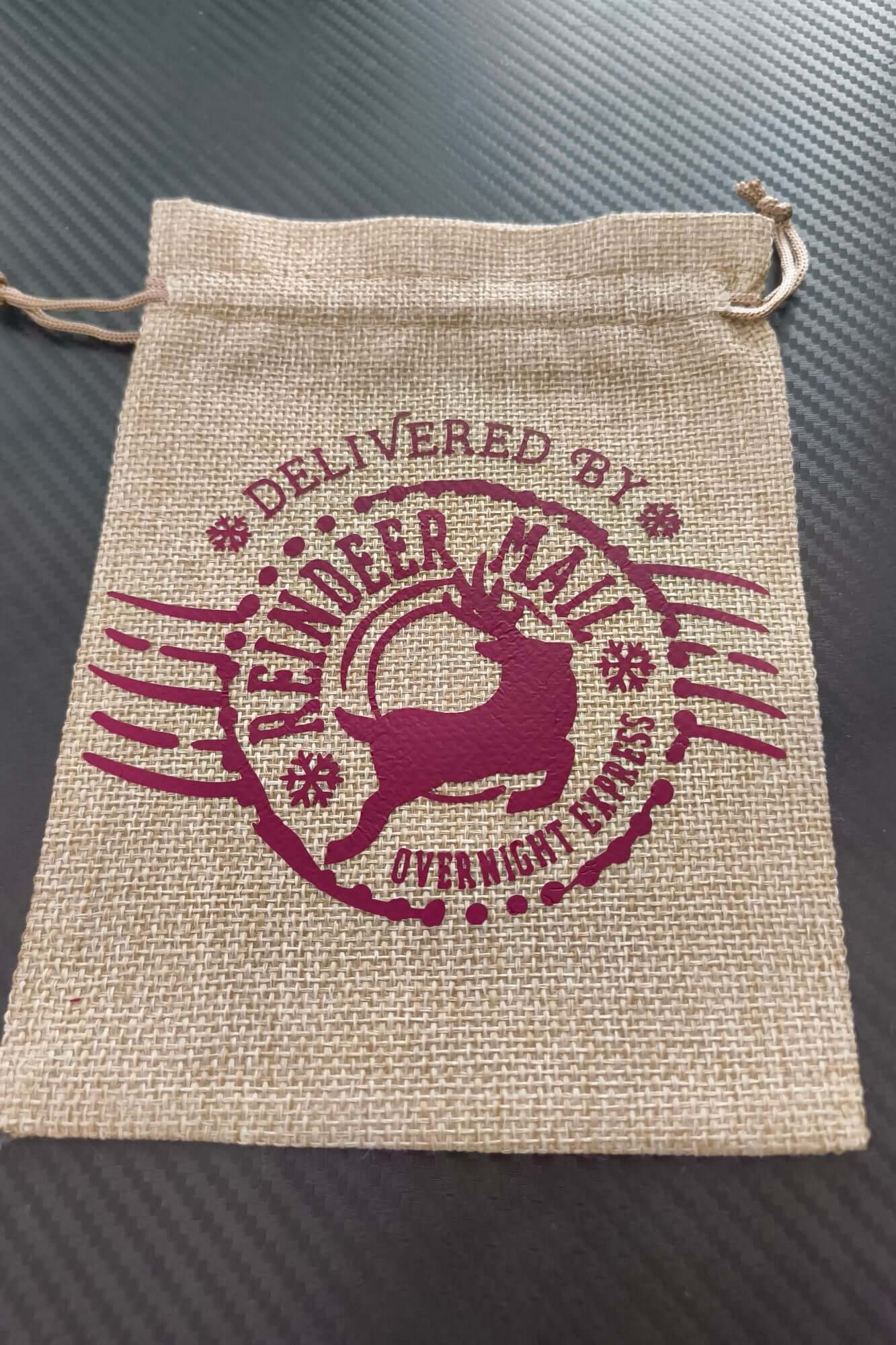 Hessian drawstring Christmas gift bag with festive reindeer mail print in burgundy, flat and ready for filling.
