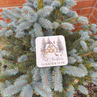First Christmas new home coaster placed on evergreen tree branches, celebrating a new home for the holidays.