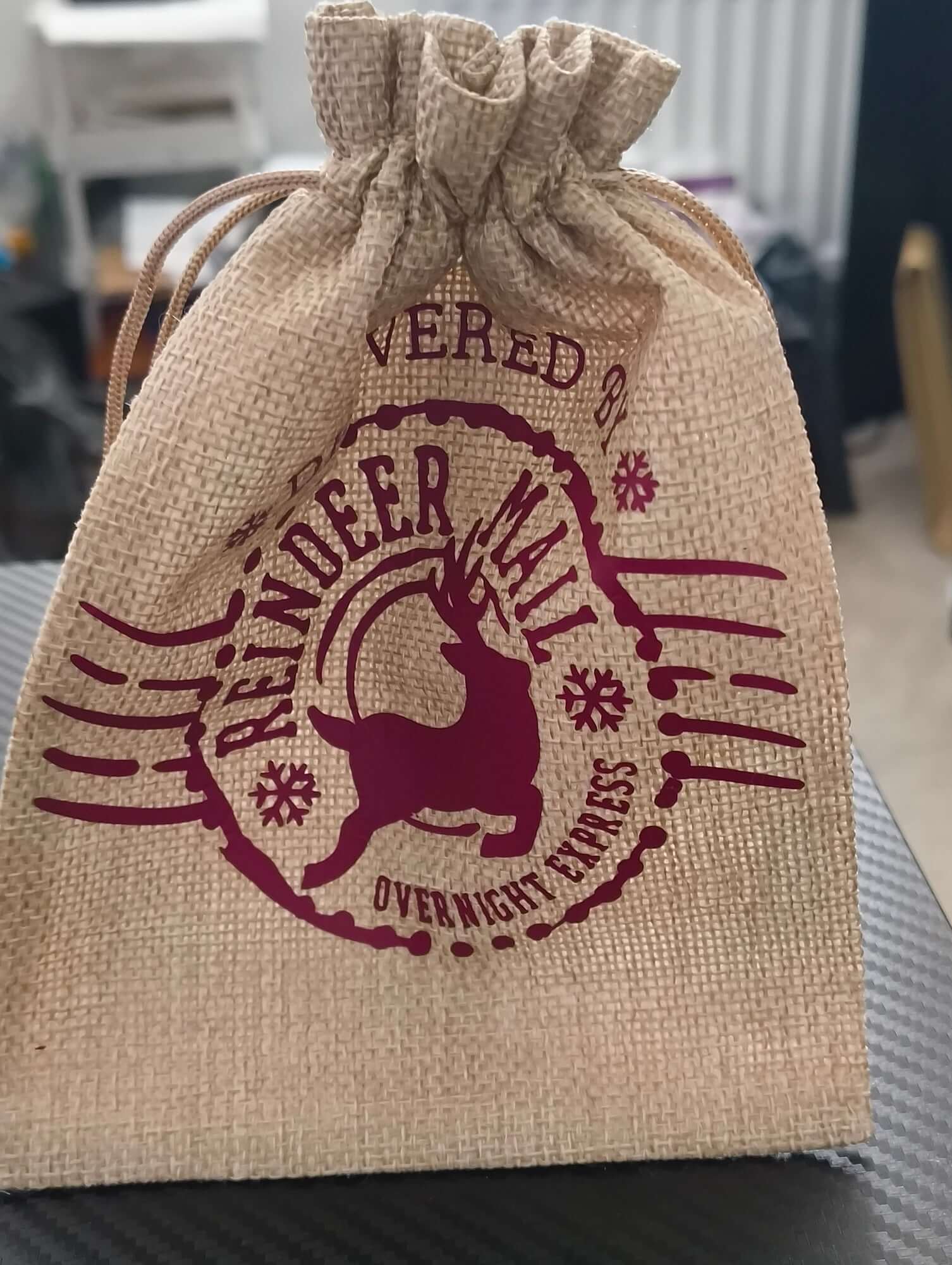 Rustic Christmas hessian bag with burgundy reindeer design, closed at the top with drawstring.