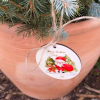Close-up of Santa Christmas bauble with custom name, tied with jute string on festive evergreen branches.