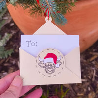 Cream envelope-shaped money holder with Santa cow design hanging on Christmas tree branch