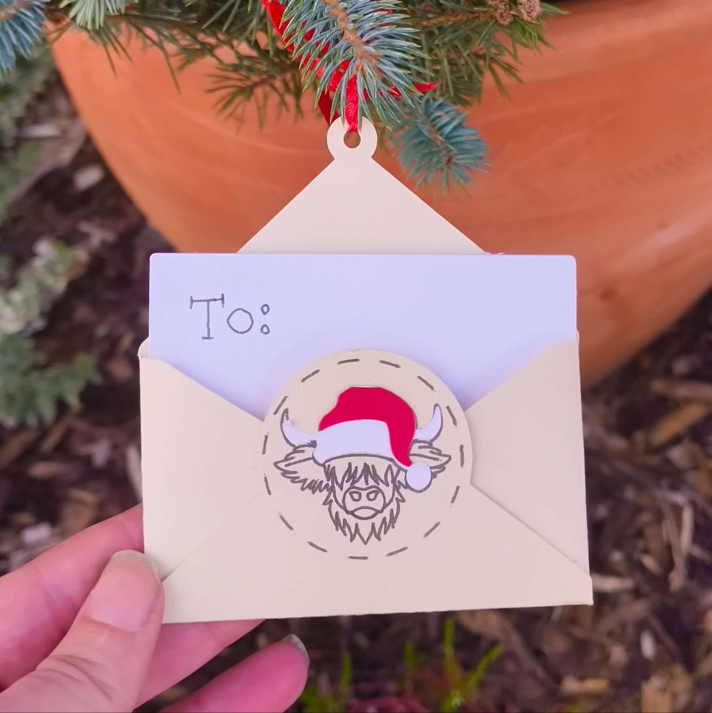 Cream envelope-shaped money holder with Santa cow design hanging on Christmas tree branch