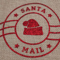 Close-up of red glitter Santa hat design and Santa Mail lettering on hessian gift bag.