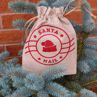Santa Mail drawstring hessian gift bag hanging on outdoor Christmas tree against brick wall.