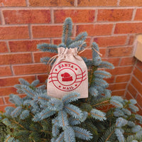 Santa Mail hessian bag with red festive print, hanging on Christmas tree branches near brick wall.
