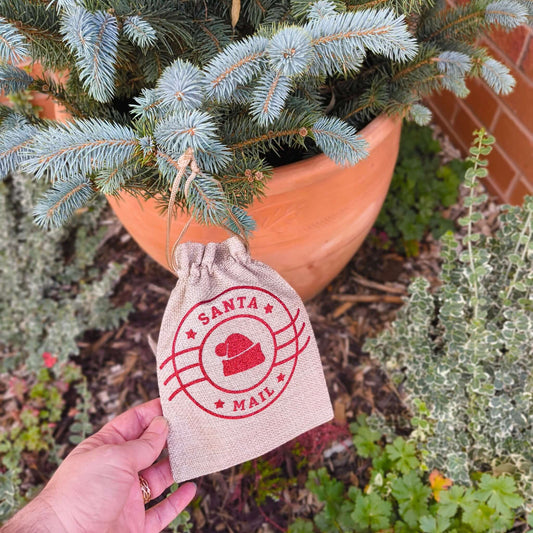 Close-up view of Santa Mail hessian sack with red festive design hanging on spruce tree branch.