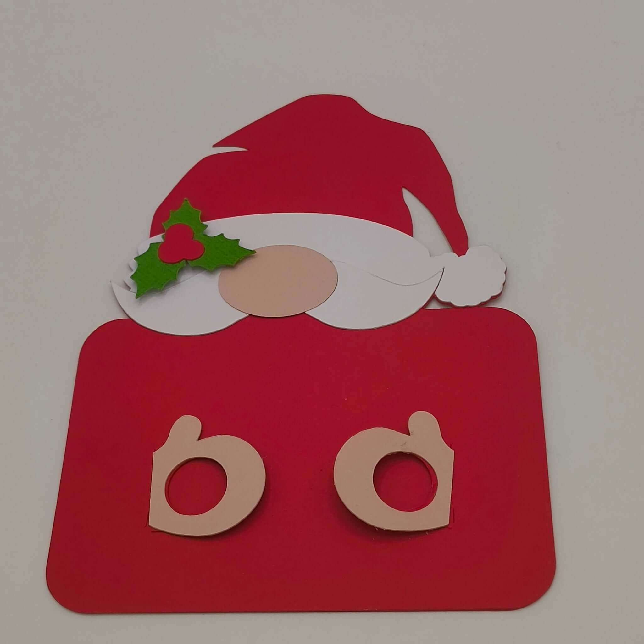 Red Santa money holder card with cut-out slots ready to hold a banknote, decorated with a paper Santa hat, beard, and holly embellishment on a plain white background.