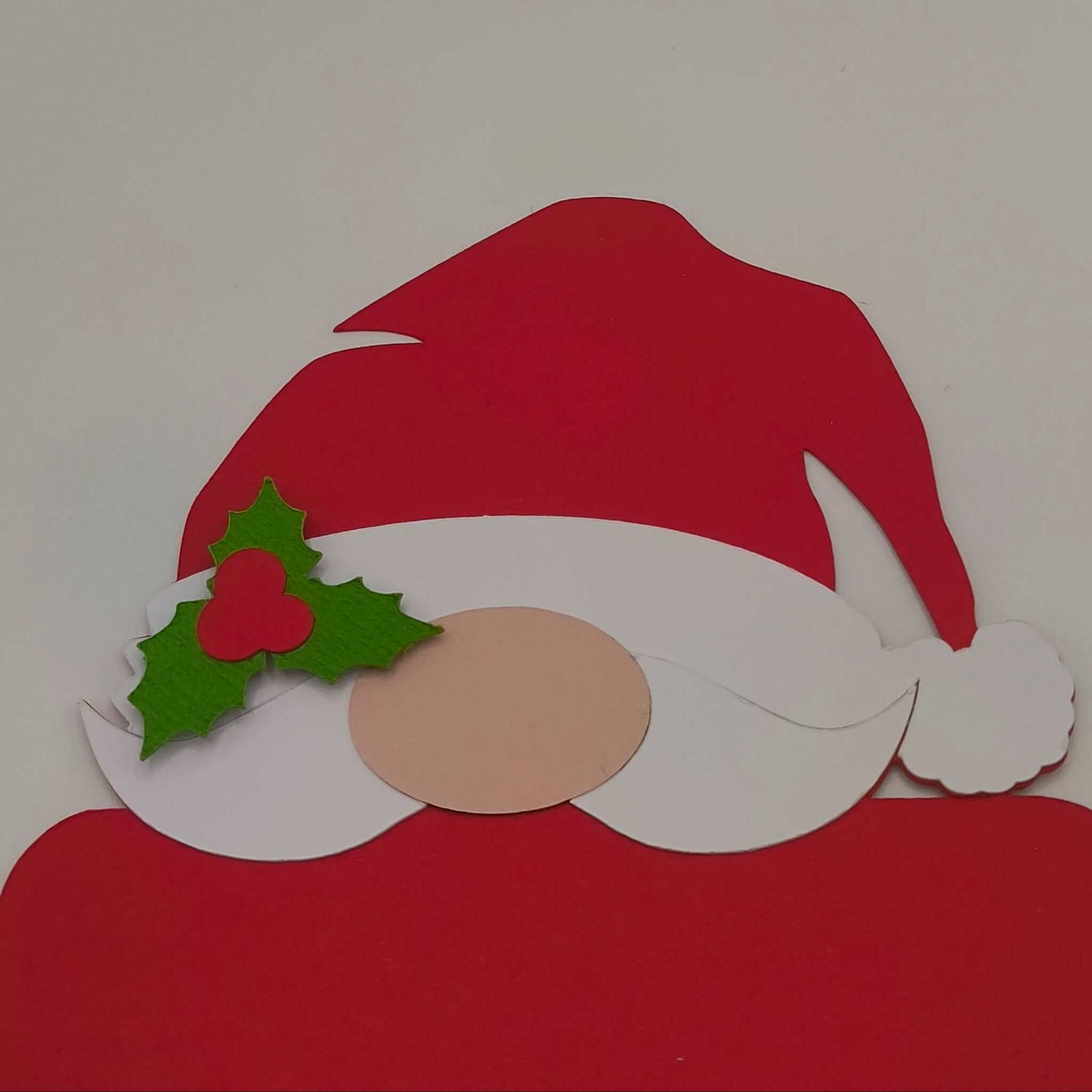 Close-up of handmade Santa money holder card, showing the red hat, white beard, and green holly detail with a festive berry on a plain background.