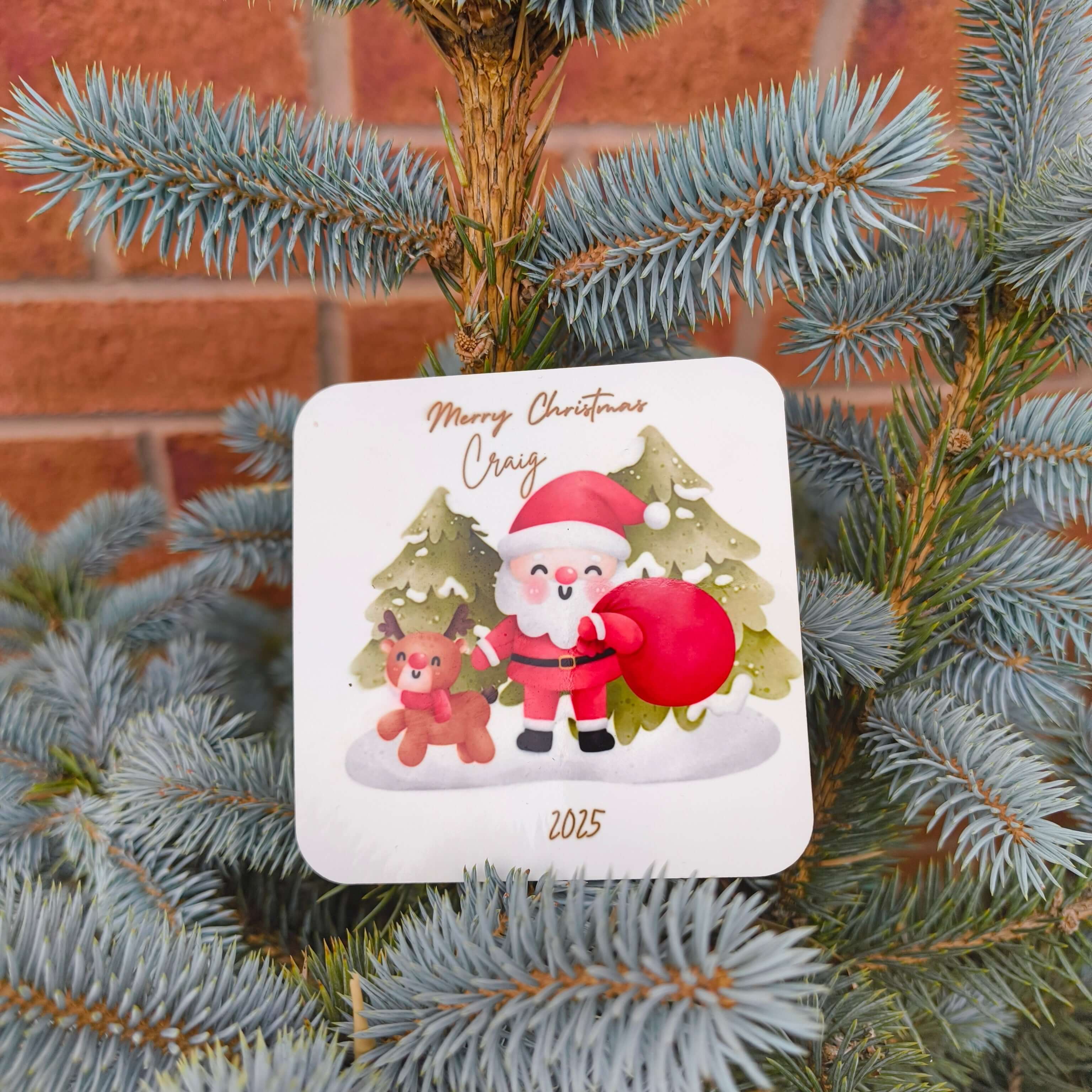Festive Santa and reindeer personalised Christmas coaster with name and year, styled outdoors on a fir tree.