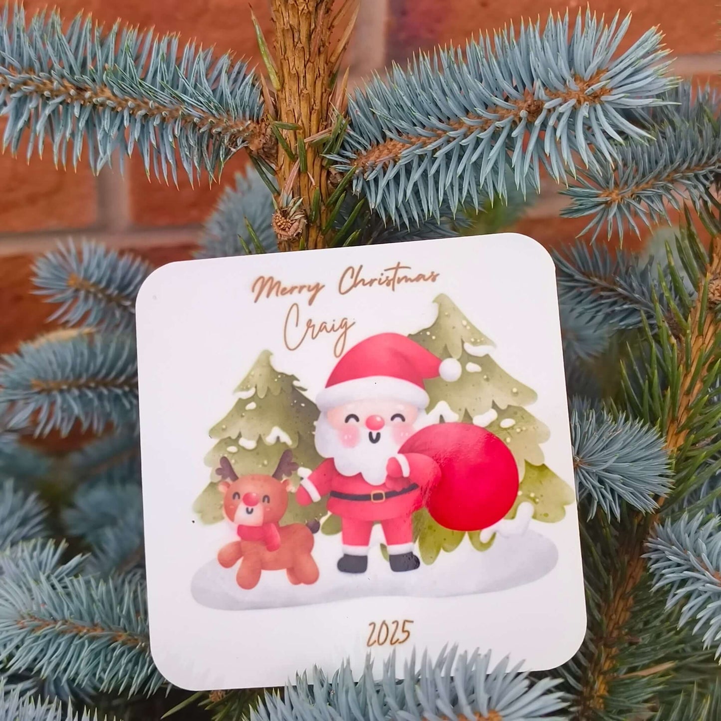 Close-up of Santa and reindeer coaster, personalised with name and year, resting among festive evergreen branches.
