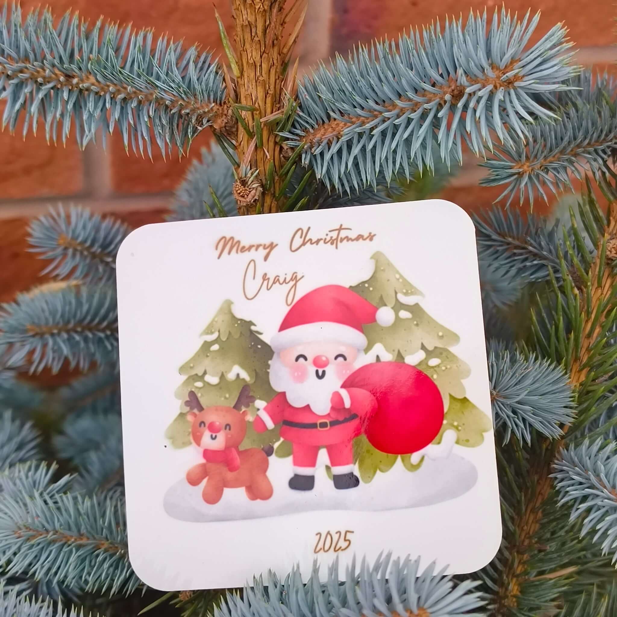 Close-up of Santa and reindeer coaster, personalised with name and year, resting among festive evergreen branches.
