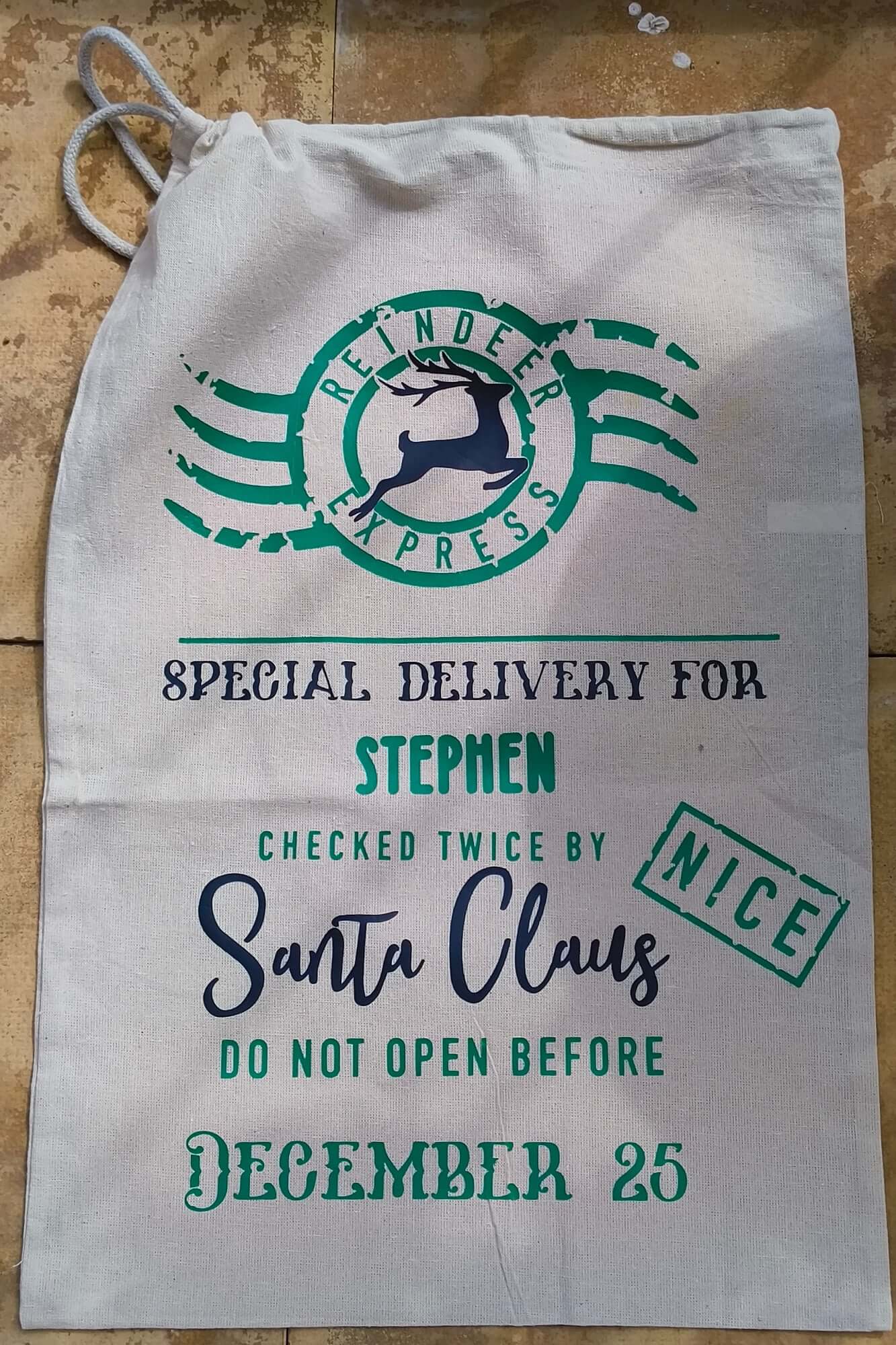 Flat lay of personalised Santa Claus sack with green and black lettering, “Special Delivery” message, and December 25 note.