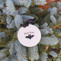 Trick or Treat Halloween bauble with black bat print, hanging on outdoor evergreen branch.