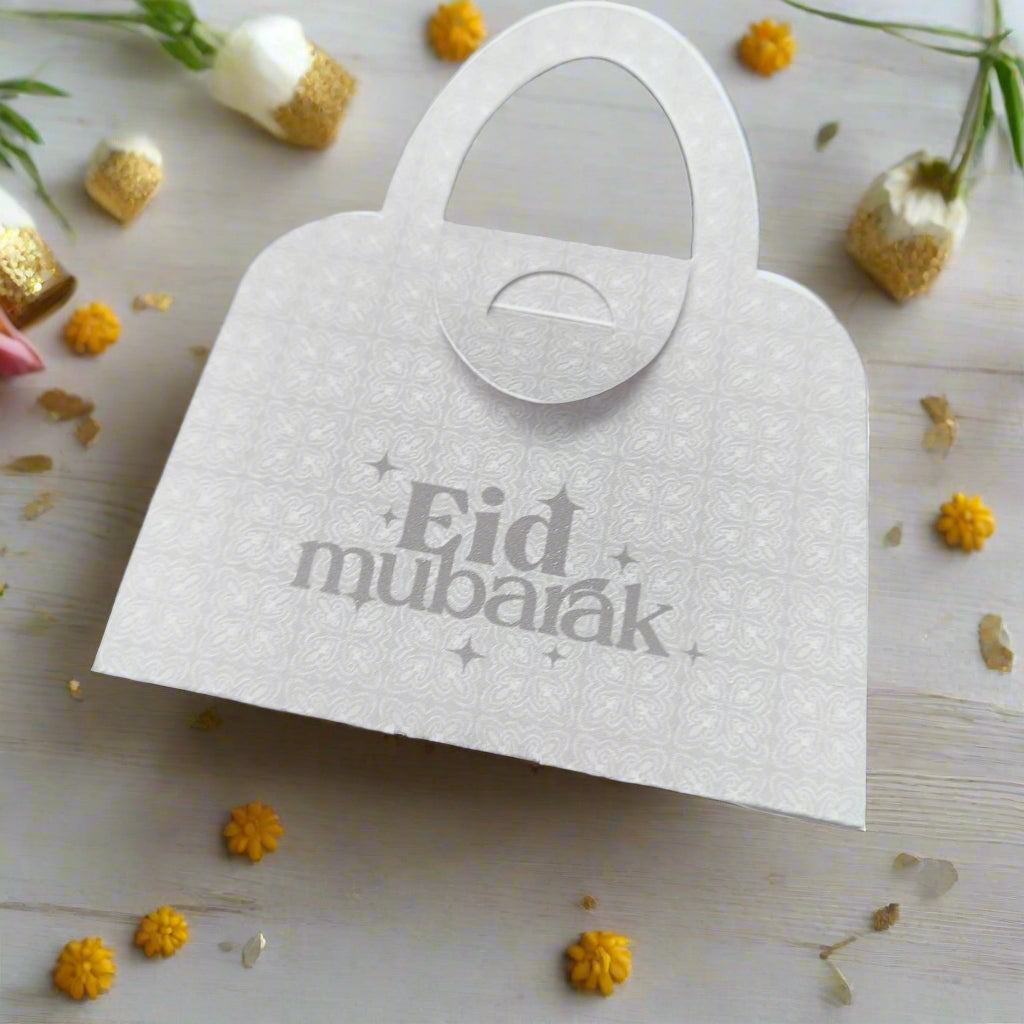 White Eid Mubarak handbag-shaped money holder with delicate floral detail, surrounded by yellow flowers, perfect Eid gift idea.