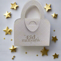 White Eid Mubarak handbag-shaped money holder with subtle pattern, decorated with golden stars for a festive touch.