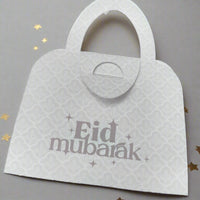 Elegant white Eid Mubarak money holder in handbag style, with delicate patterned detail and festive golden star accents.