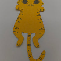 Handmade yellow paper cat cut-out with drawn stripes, big eyes, and a long tail on a white background.